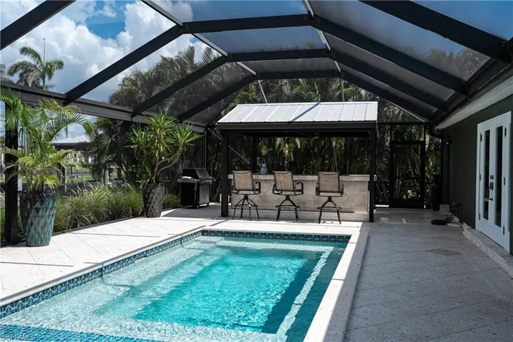 Outdoor pool with a sunroom, a patio area, a grill, and a lanai