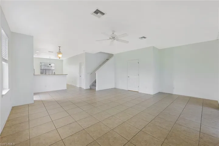 Unfurnished living room featuring ceiling fan, light tile patterned flooring, and stairway