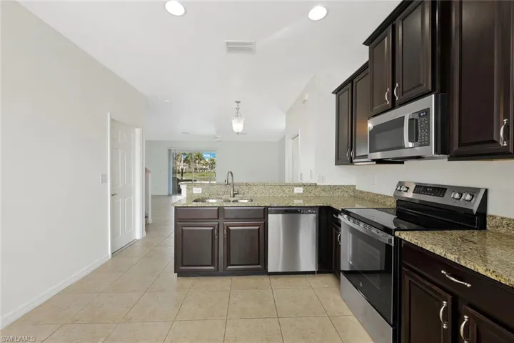 Kitchen featuring stainless steel appliances, dark brown cabinetry, light stone counters, decorative light fixtures, and a peninsula
