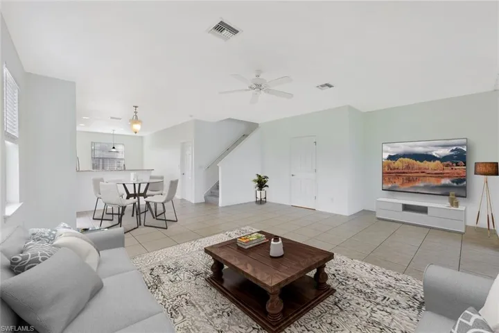 Living room featuring light tile patterned floors, a ceiling fan, and stairs