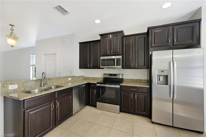 Kitchen featuring appliances with stainless steel finishes, light stone countertops, dark brown cabinets, hanging light fixtures, and a peninsula
