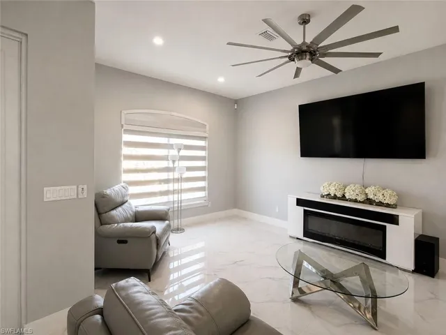 Recessed ceiling lighting, large ceiling fan, built-in fireplace feature, bright window with blinds, and polished tile flooring