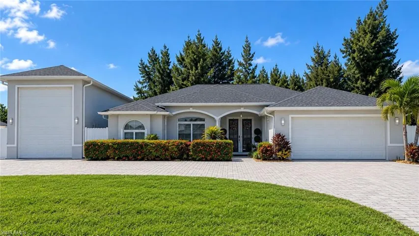 Stucco exterior with a dark shingle roof, arched entryway, and a paver driveway