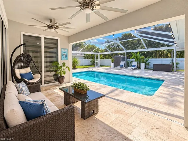 Screened-in patio with multiple ceiling fans, featuring a rectangular swimming pool, light-toned stone-finish decking, and sliding glass doors
