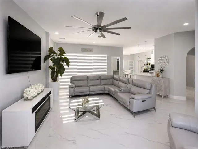 Recessed lighting, large format tile flooring, modern ceiling fan, built-in electric fireplace, and an arched doorway