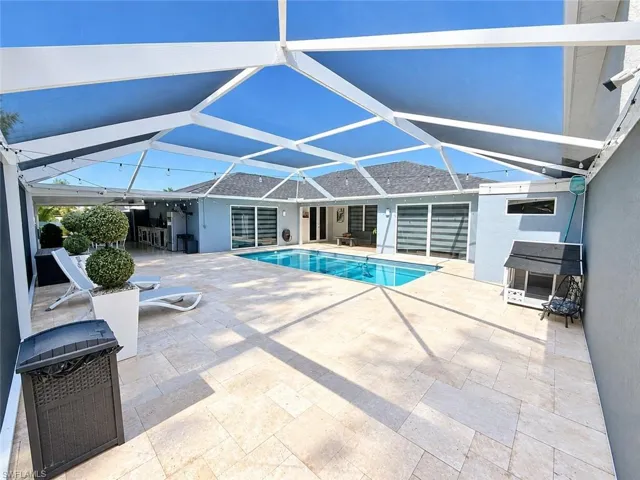 Screened-in outdoor living space with a swimming pool, expansive paver patio, and covered outdoor kitchen area