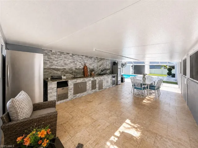 Expansive covered patio featuring a full outdoor kitchen, built-in stainless steel appliances, natural stone backsplash, and neutral-toned tile flooring