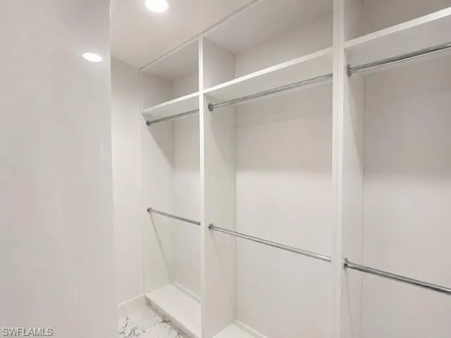 Custom closet system featuring multiple shelves, hanging rods, recessed lighting, and a marble-finish floor