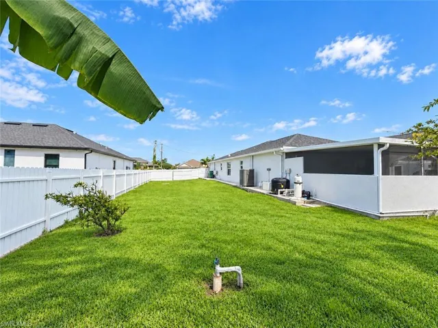 Expansive backyard featuring a green lawn, white privacy fencing, and a screened patio