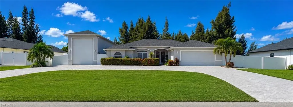 Expansive paver driveway, manicured lawn, and lush landscaping frame the property