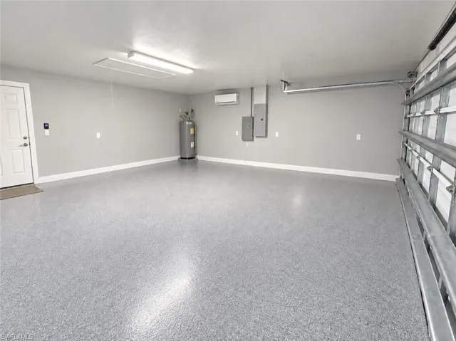 Spacious garage with light gray speckled flooring, white interior door, water heater, and wall-mounted air conditioning unit