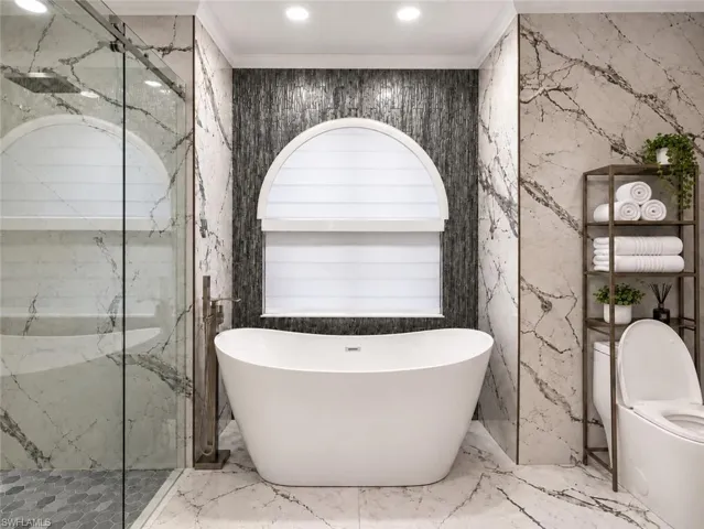 Freestanding soaking tub with floor-mounted fixture, glass-enclosed shower with mosaic tile floor, and large format wall tile