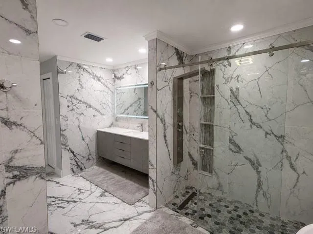 Full wall and floor tile with veining, vanity with single basin, illuminated mirror, walk-in shower with sliding glass door, and recessed shower niche