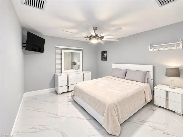 Marble-look tile flooring, ceiling fan with integrated lighting, wall-mounted television, and a built-in hanging rack