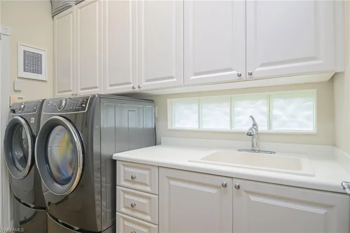 Clothes washing area featuring sink, washer and dryer, and cabinets