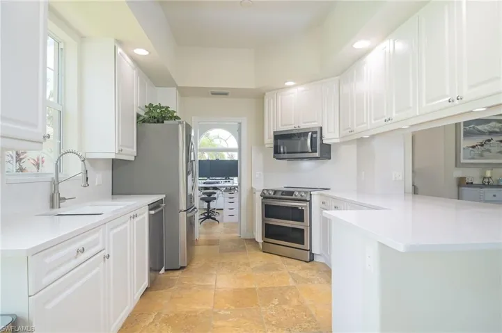 Kitchen with white cabinetry, stainless steel appliances, light tile flooring, and sink