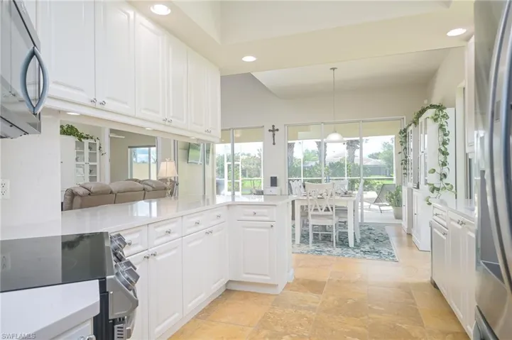 Kitchen with decorative light fixtures, white cabinets, light tile flooring, kitchen peninsula, and appliances with stainless steel finishes