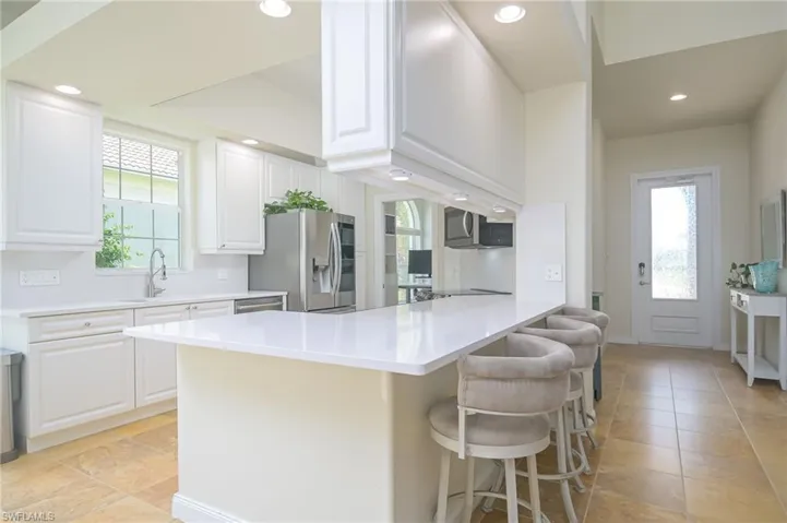 Kitchen featuring plenty of natural light, a breakfast bar, light tile flooring, and stainless steel refrigerator with ice dispenser