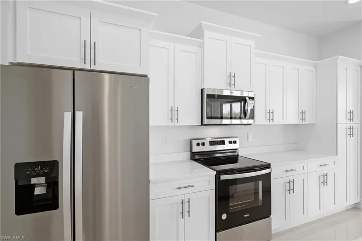 Kitchen with stainless steel appliances, white cabinets, and light tile flooring