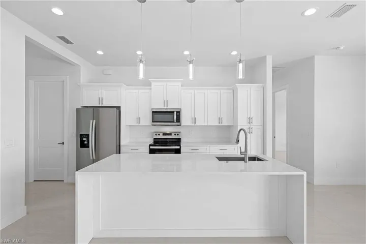 Kitchen with stainless steel appliances, a center island with sink, sink, and light tile floors