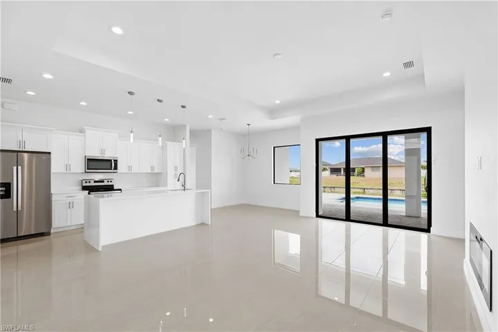 Kitchen with decorative light fixtures, stainless steel appliances, a raised ceiling, an island with sink, and light tile floors