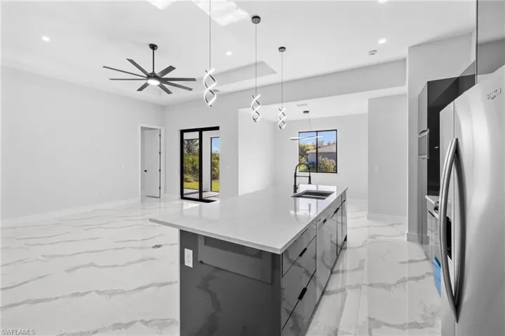 Kitchen with light stone countertops, stainless steel fridge, ceiling fan, sink, and a large island