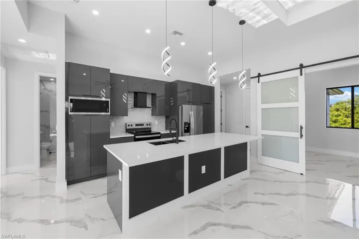 Kitchen featuring stainless steel appliances, sink, a barn door, hanging light fixtures, and an island with sink