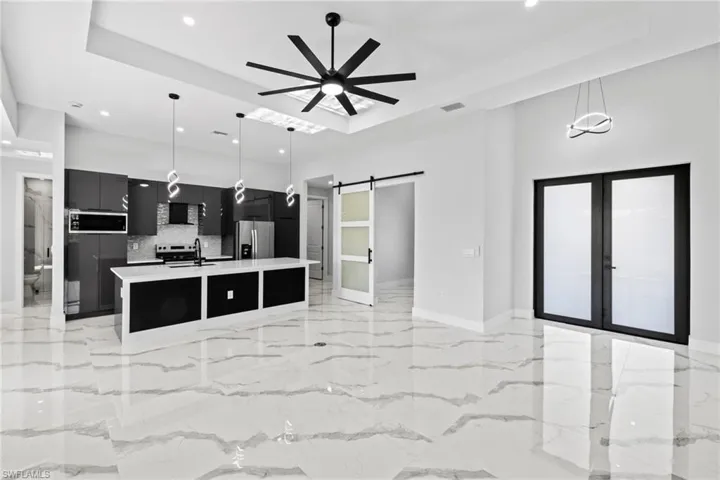 Kitchen featuring ceiling fan, a barn door, pendant lighting, a kitchen island with sink, and appliances with stainless steel finishes