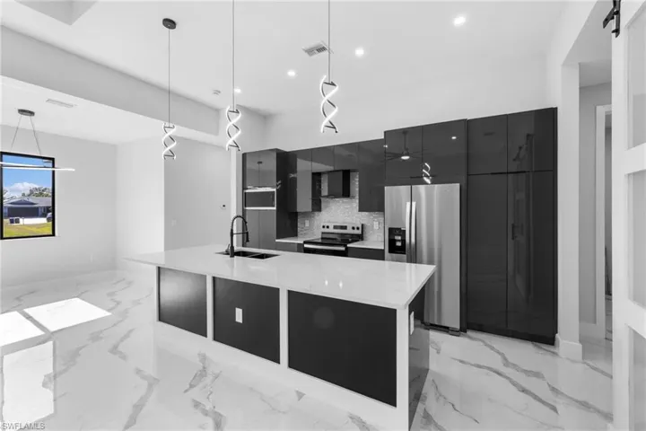 Kitchen with tasteful backsplash, stainless steel appliances, a kitchen island with sink, sink, and decorative light fixtures