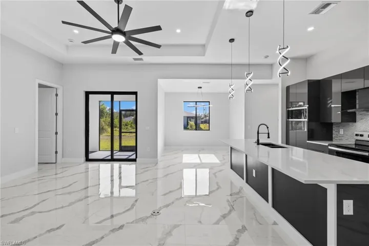 Kitchen with a large island with sink, backsplash, decorative light fixtures, and ceiling fan