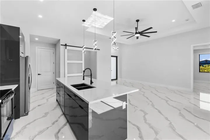 Kitchen featuring stainless steel refrigerator, a large island, sink, light stone countertops, and decorative light fixtures