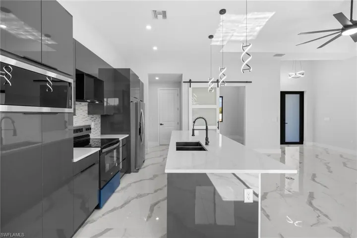 Kitchen with sink, a barn door, a spacious island, decorative light fixtures, and appliances with stainless steel finishes