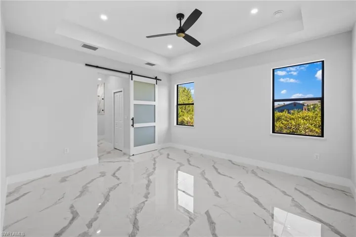 Empty room with a barn door, a tray ceiling, and ceiling fan