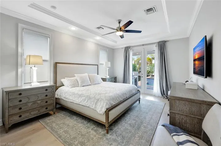 Bedroom with crown molding, a tray ceiling, light hardwood / wood-style floors, access to outside, and french doors