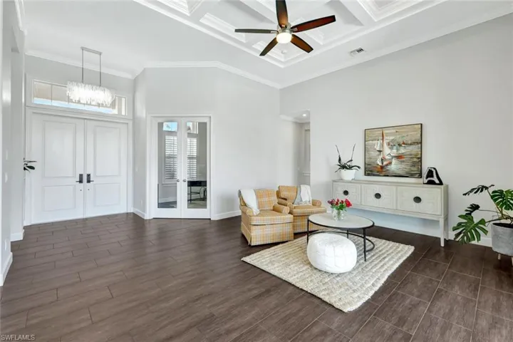 Sitting room featuring coffered ceiling, ornamental molding, dark hardwood / wood-style flooring, ceiling fan with notable chandelier, and french doors