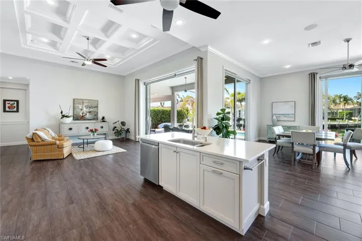 Kitchen featuring white cabinetry, sink, coffered ceiling, stainless steel dishwasher, and a center island with sink