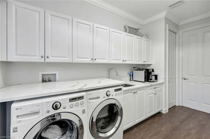 Washroom with dark wood-type flooring, sink, crown molding, cabinets, and washing machine and dryer