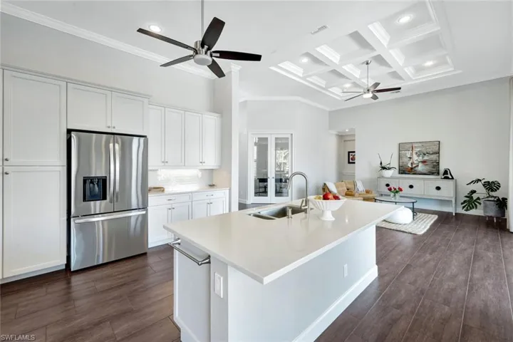 Kitchen with stainless steel refrigerator with ice dispenser, coffered ceiling, sink, a center island with sink, and white cabinets