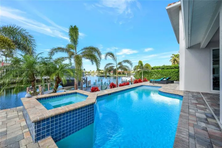 View of swimming pool featuring a patio, a water view, and an in ground hot tub