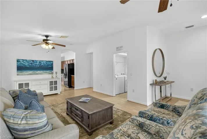 Living room with ceiling fan, washing machine and dryer, arched walkways, and light wood-style floors