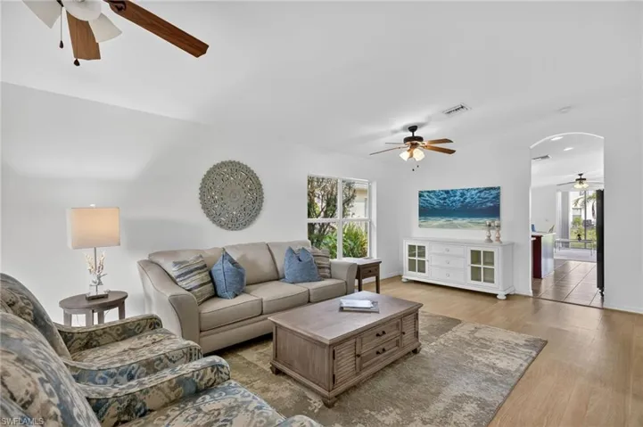Living room with a ceiling fan, light wood finished floors, and arched walkways