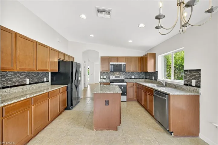Kitchen with backsplash, arched walkways, stainless steel appliances, a kitchen island, and vaulted ceiling