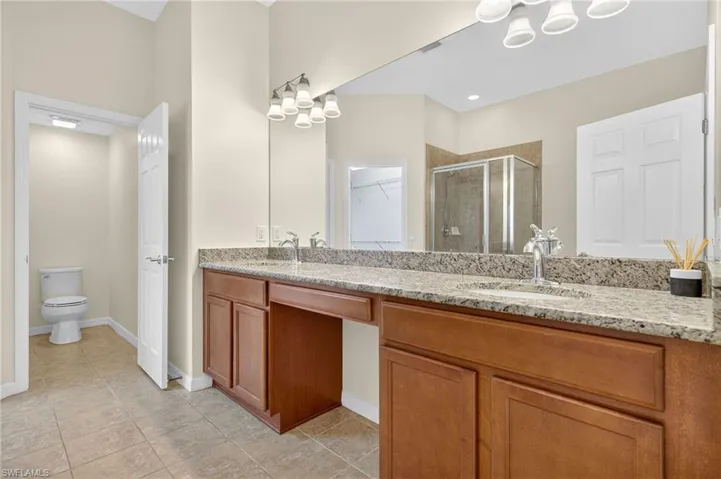Bathroom featuring a shower stall, double vanity, a spacious closet, tile patterned floors, and a chandelier