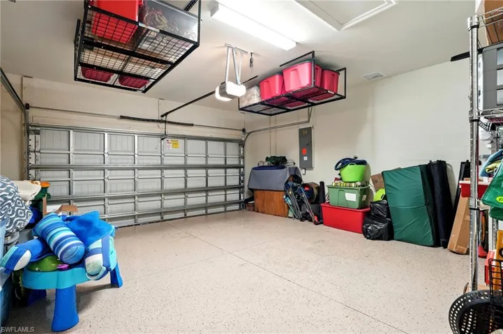 Garage featuring a textured concrete floor, panel garage door, integrated overhead storage racks, and overhead lighting