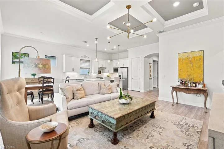 Coffered ceiling with a modern chandelier, wood-finish flooring, recessed lighting, white shaker cabinetry, and an arched doorway