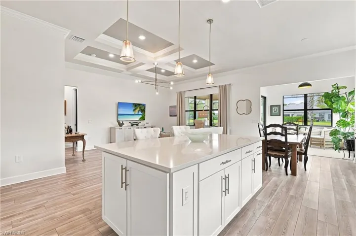 Kitchen island with white cabinetry and light-toned countertop, wood-finish flooring, coffered ceiling with recessed lighting, and pendant light fixtures