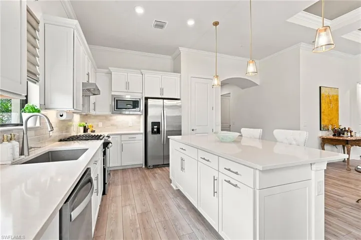 Modern kitchen featuring white cabinetry, stainless steel appliances, light-toned countertops, wood-finish flooring, and a central island with pendant lighting