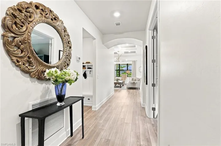 Wood-finish flooring throughout, white wall finishes, built-in mudroom bench, arched doorway, and recessed lighting