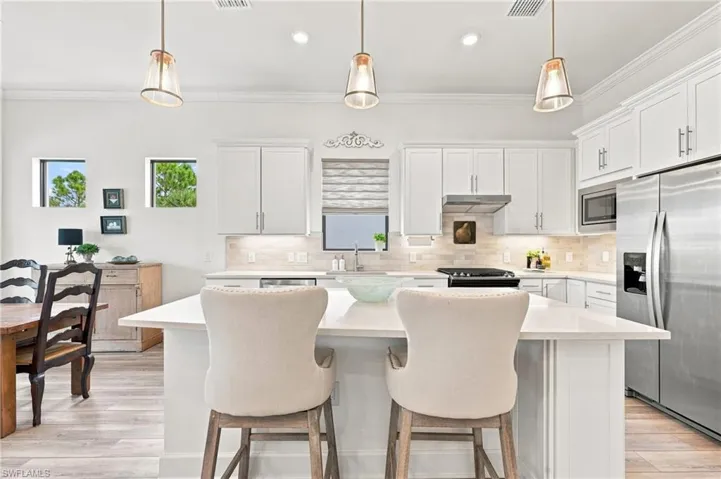 White shaker cabinetry, stainless steel appliances, central island with seating, pendant lighting, and wood-finish flooring