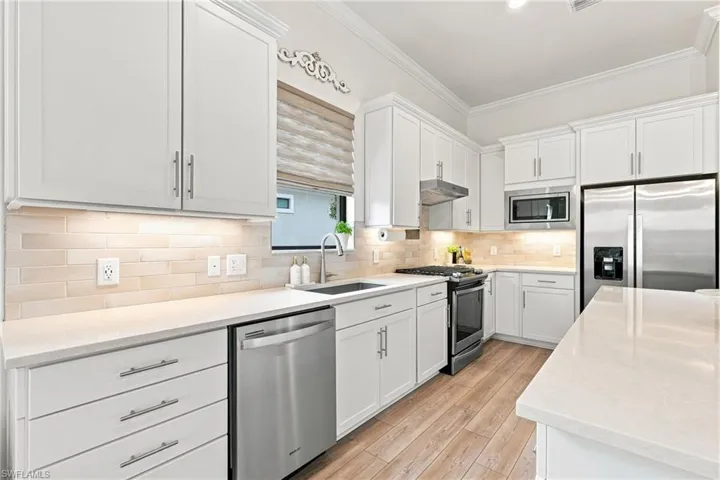 White shaker cabinetry with brushed nickel hardware, stainless steel appliances, wood-finish flooring, undermount sink, and light-toned backsplash